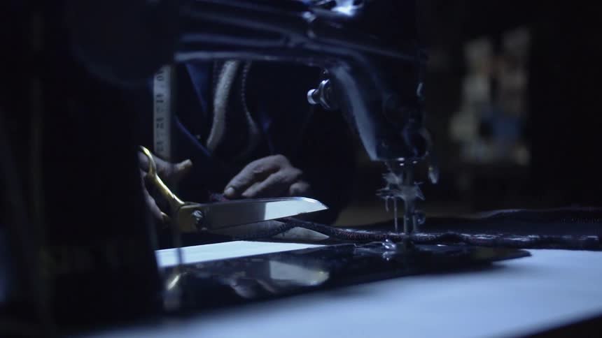 A person with a measuring tape cutting a piece of cloth with a scissors next to a sewing machine
