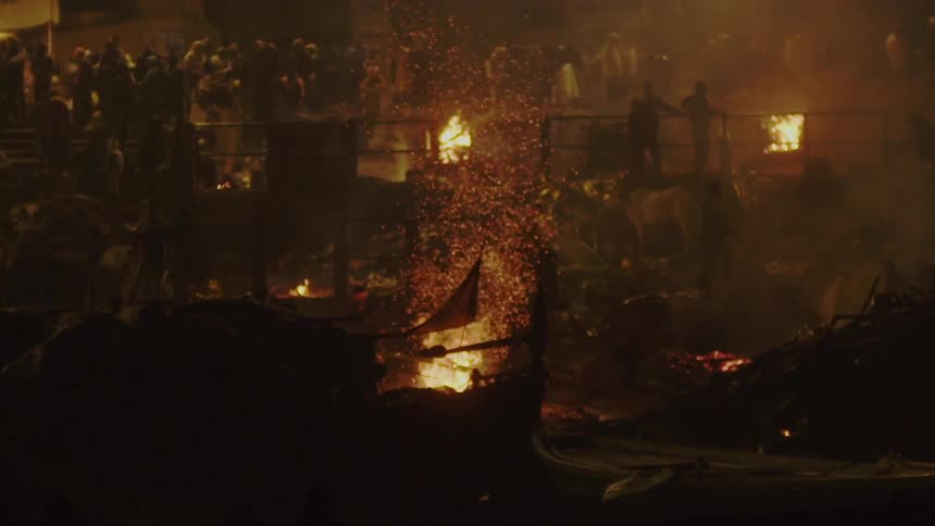 A person on a rowboat with fire embers and people in the background