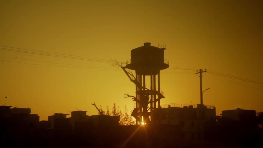 Sun setting in the distance behind a silhouetted water tower
