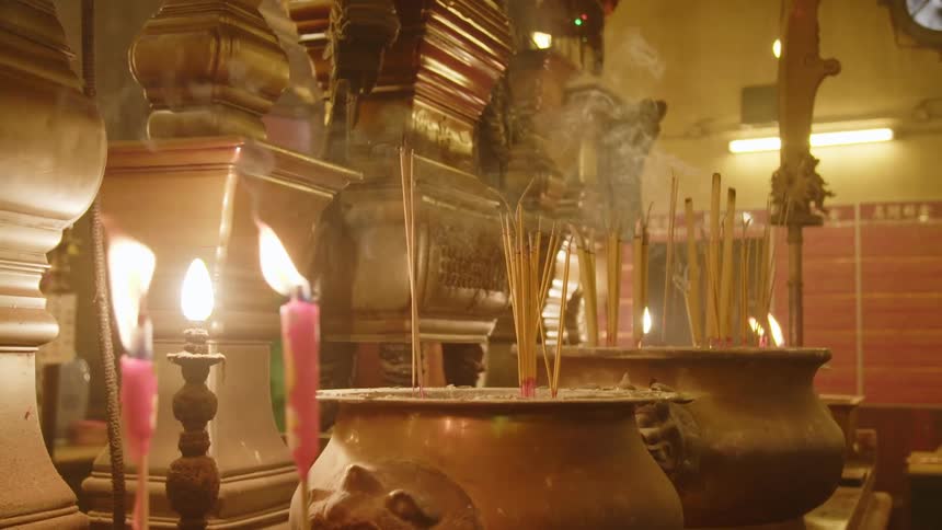 Several candles and sticks of incense burn inside of a temple
