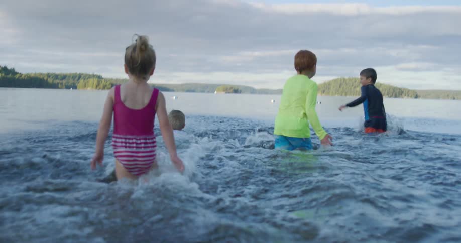Kids run into shallow water as wide cloud bank covers promontory on opposite shore