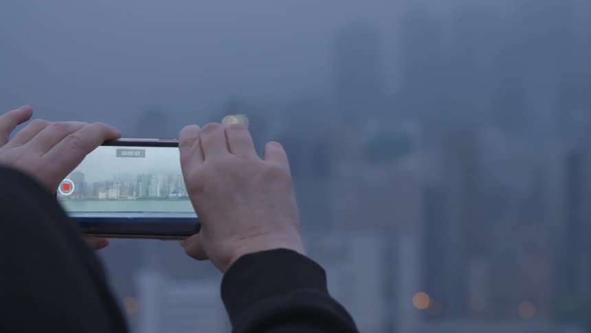 A man takes a video on his cell phone of a city skyline