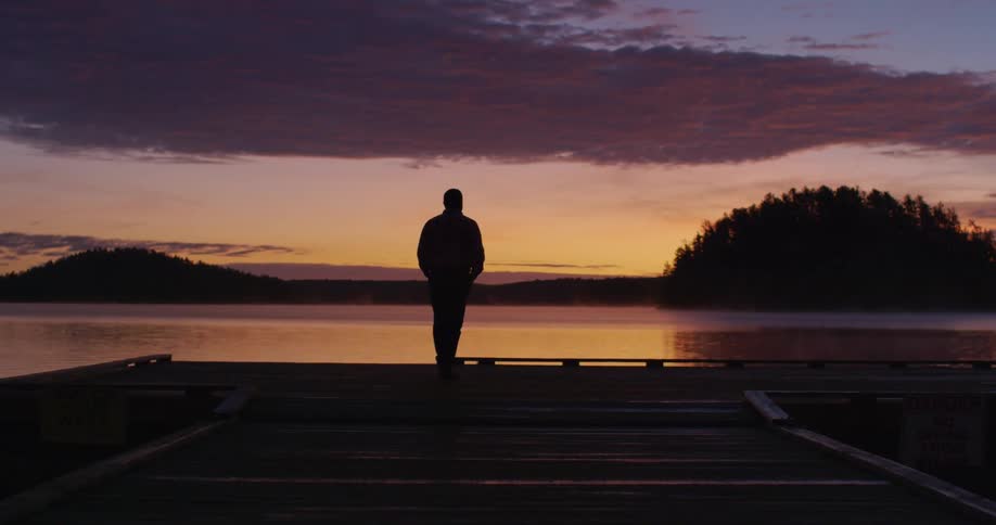 A man walks to the edge of a dock and looks out at the water