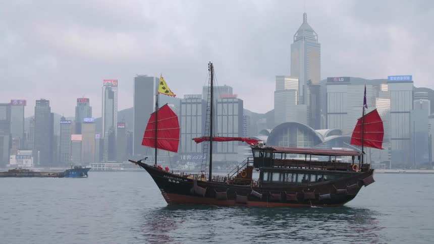 A ferry with red sails passes by tall skyscrapers