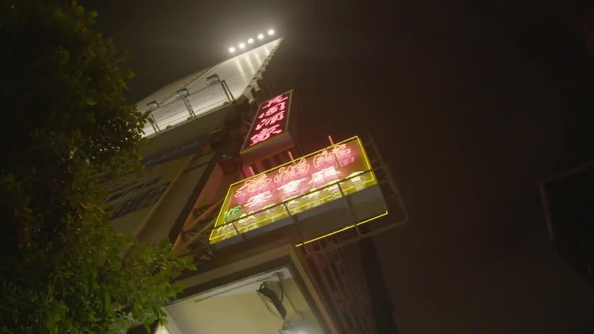 A camera points straight up at neon light business signs and a billboard lit for night