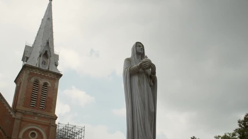 Statue of a female saint outside of a church with a bell tower