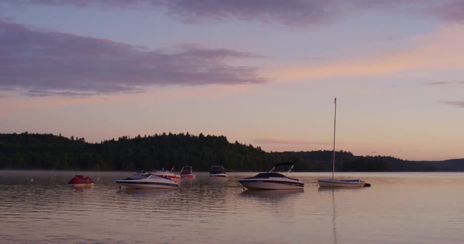 Boats and a jet ski parked out on a body of water in front of a sunset horizon