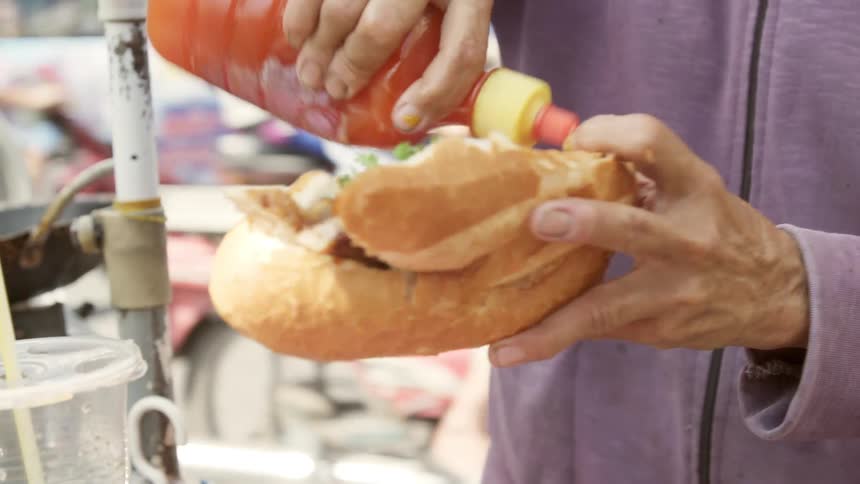 A person putting sauce on a sandwich