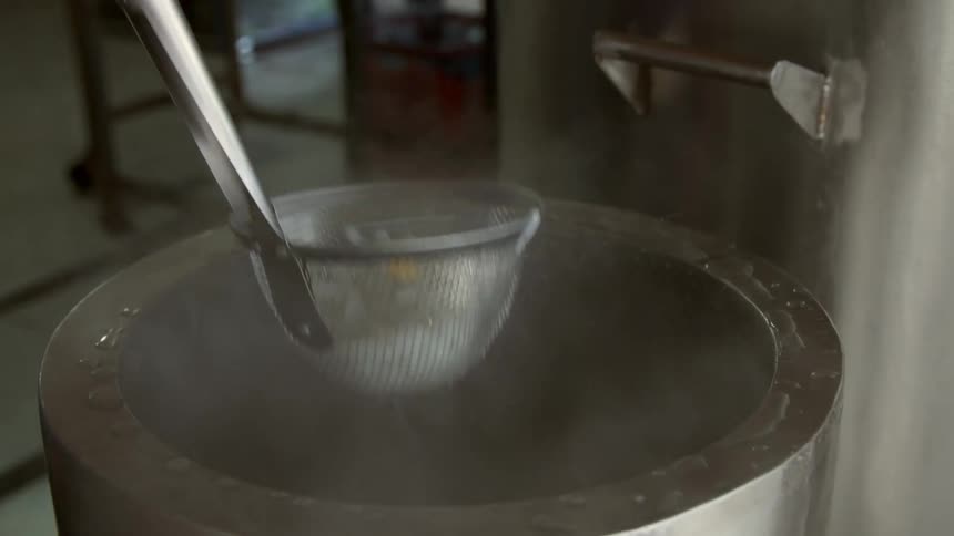 Noodles being removed from a pot of water with a strainer