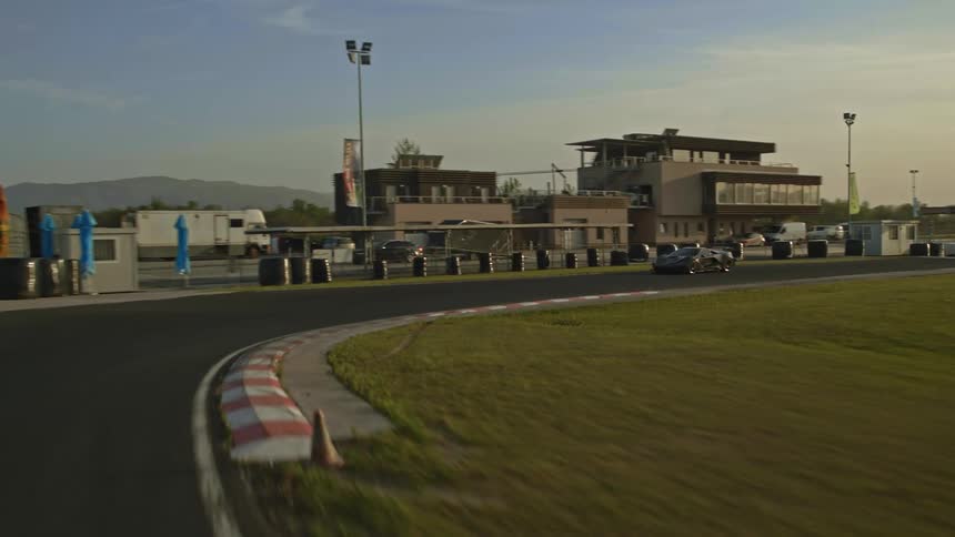 A car is driving on a racetrack at dusk