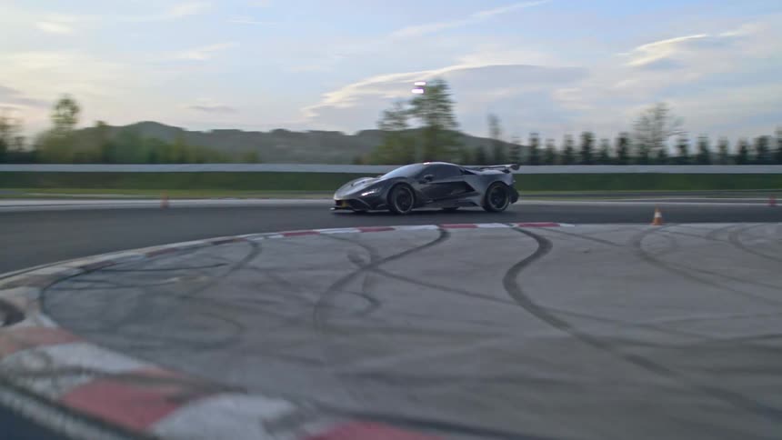 A black sports care is driving on a curved portion of a race track at dusk outdoors