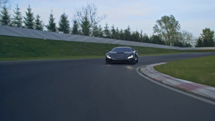 A sports car driving on a track with trees the sky and clouds in the background