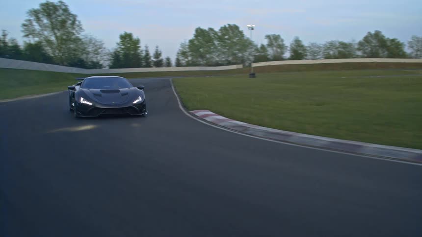 Car drives along track bordered by grass and wall