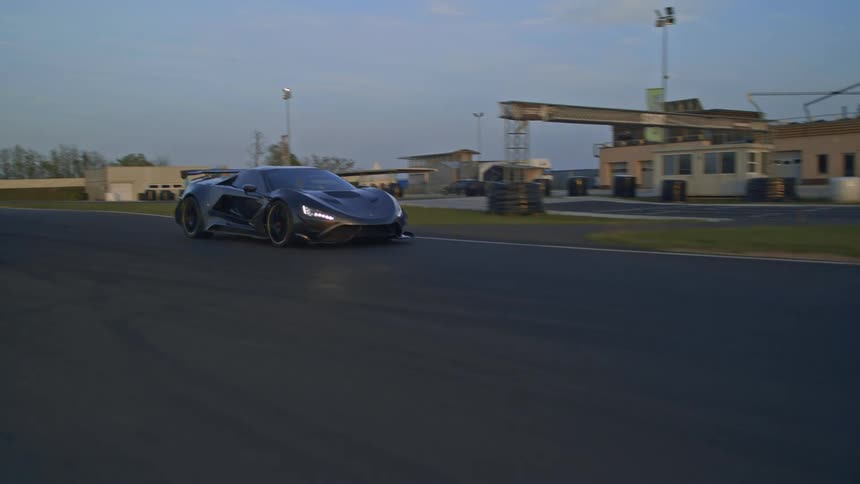A car is driving on a racetrack at dusk