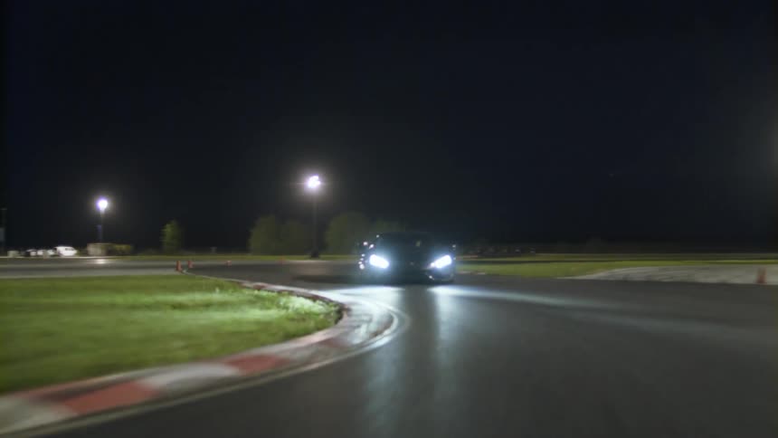 A car is driving on a racetrack at night
