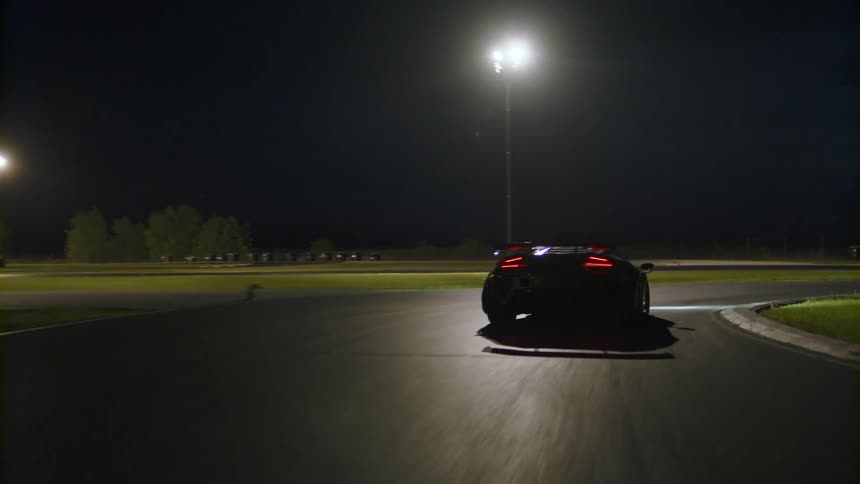 A car is driving on a racetrack at night