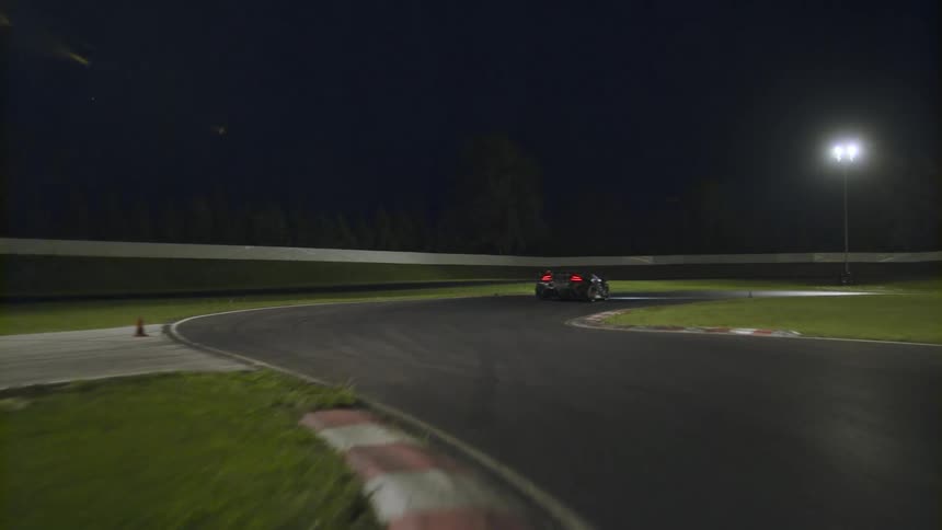 A black sports car speeds along a curved race track at night