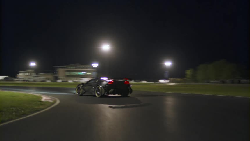 A black sports car drives on a curvy track at night