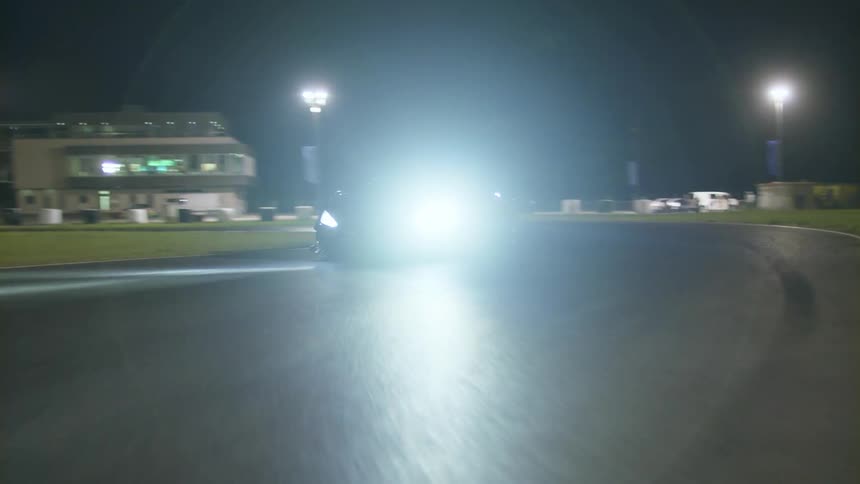 A sports car driving on a track with buildings trees and the sky in the background