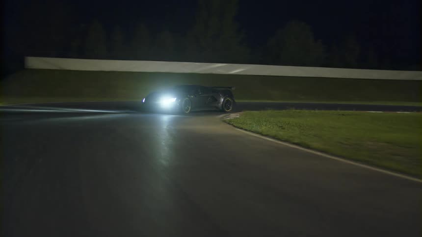 Sports car driving at night time on a racetrack next to a grass