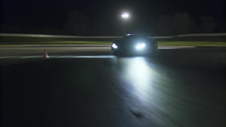 A black sports car drives a curved track at night