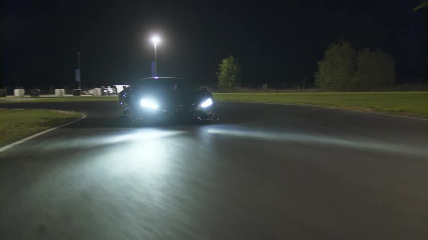 A black sports car drives on a windy track at night