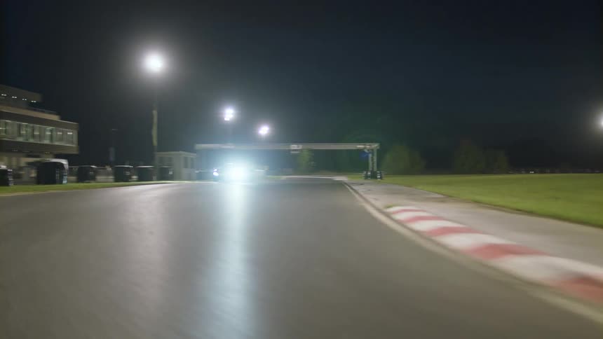 A car is driving on a racetrack at night
