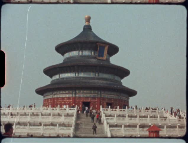 An asian temple in black red gold and blue sits with stairs in front and many people
