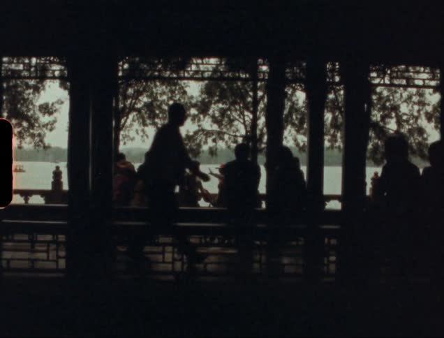 People look out over a lake from a roofed walkway on its shore