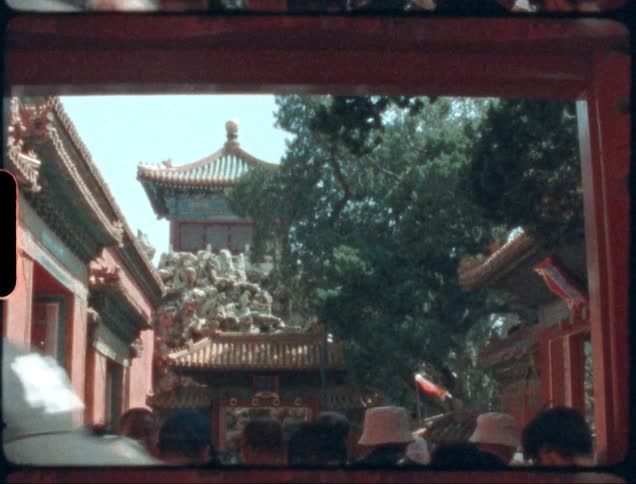 Pedestrians walk down a busy path between buildings near a pagoda