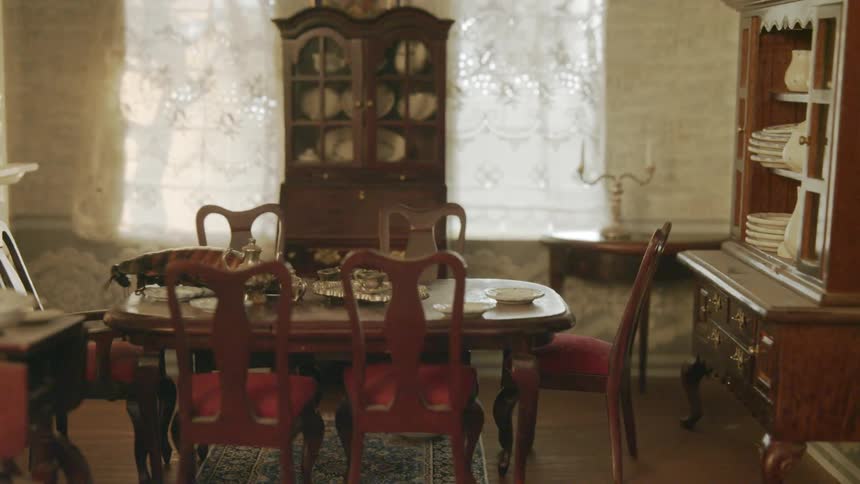 A cockroach walks across a dining room table in a doll house and knocks items over