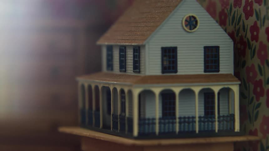 A miniature blue house sits on a table against floral wallpaper