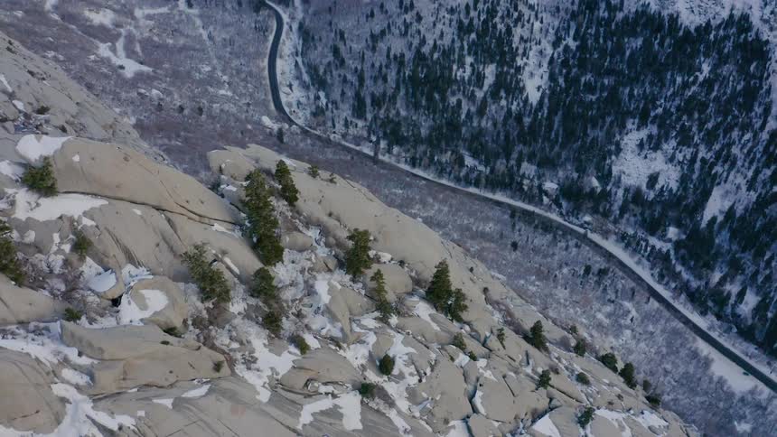 A mountain slope powdered with snow looms over a road through the valley below