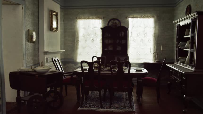 A room with a dining table and chairs with a wall and windows in the background
