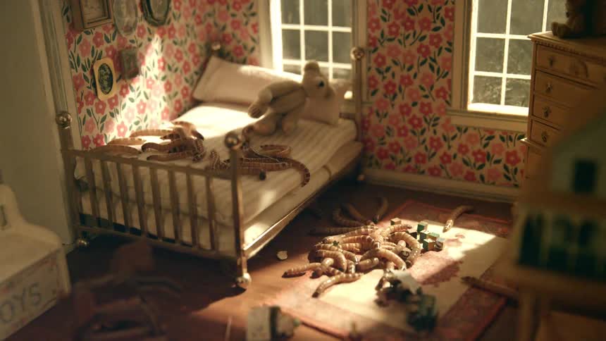 Maggots crawl within a doll house as a light moves back and forth outside the dollhouse window