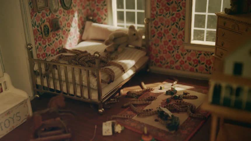 Lights sweep through interior of dollhouse as caterpillars crawl across miniature rug and carpeting