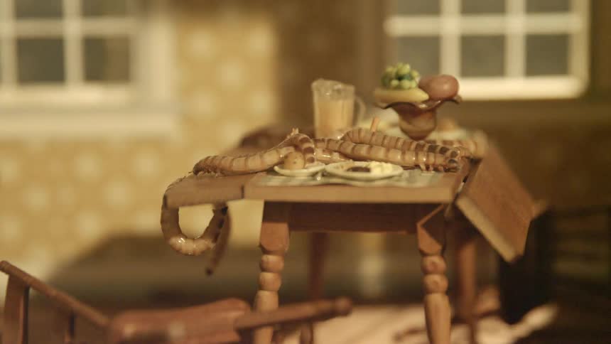 An interior of a dollhouse with a swinging light and maggots crawling on a miniature dining table