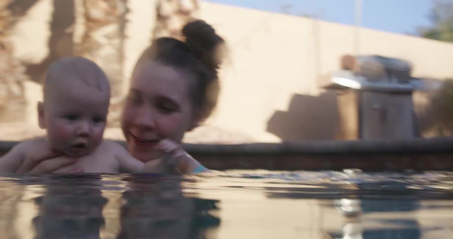 A mother holds her baby in a pool during the day