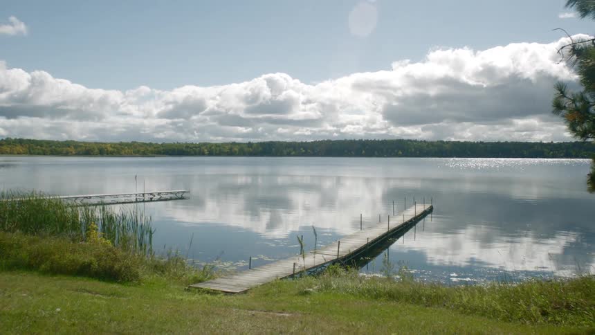 Sky reflects off lake near pier across from forest