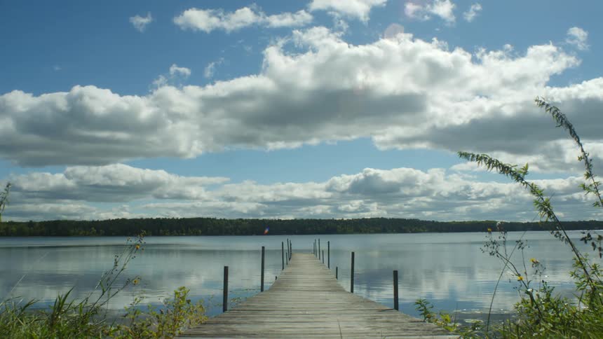 Dock extending out to water with the clouds and blue sky reflecting on the water