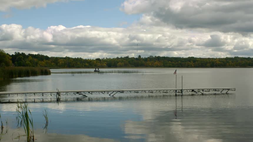 Two people sit in a canoe in a large reflective lake surrounded by dense trees