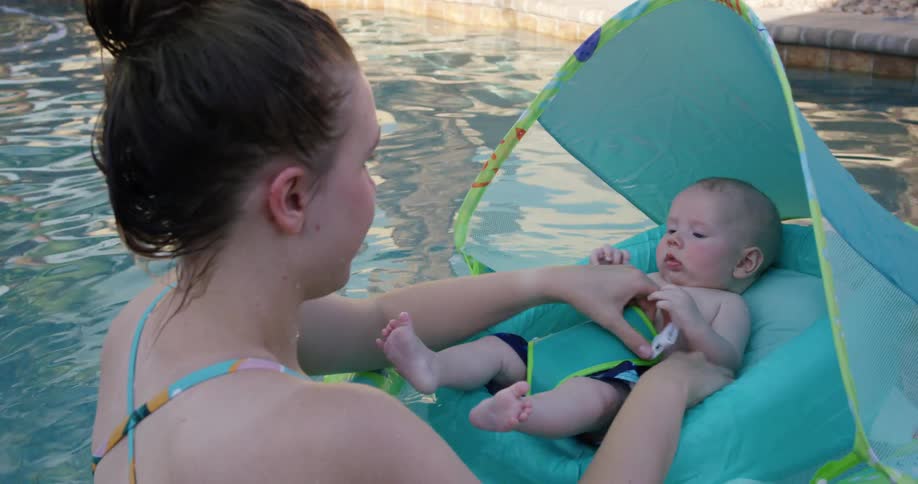 A mother straps her baby into a flotation device in an outdoor pool
