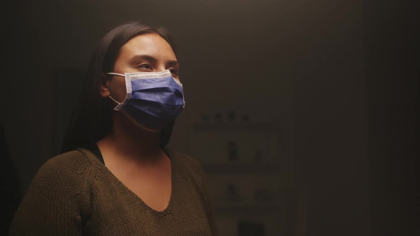 A woman is standing in a room and wearing a face mask
