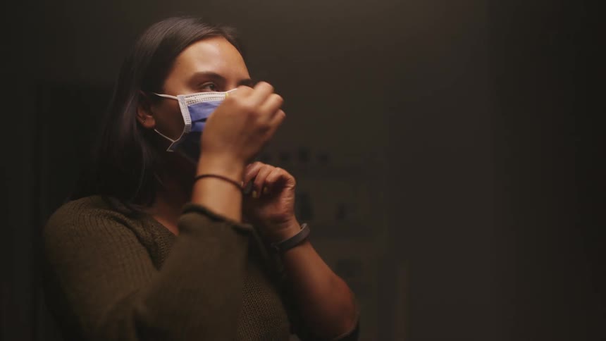 Brunette woman with short straight dark hair puts on a blue mask