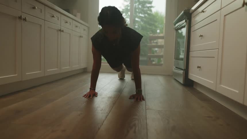 A woman does push ups on her kitchen floor