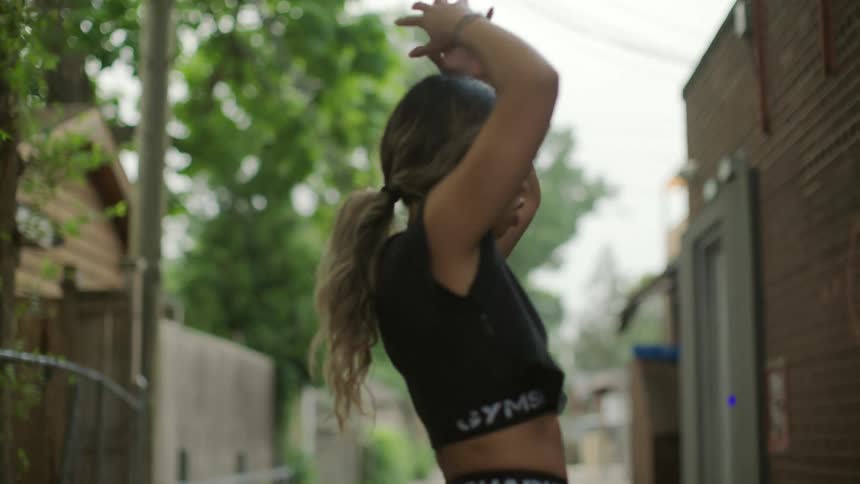 A woman walks in an alley stretching her arms and putting them to her head in distress