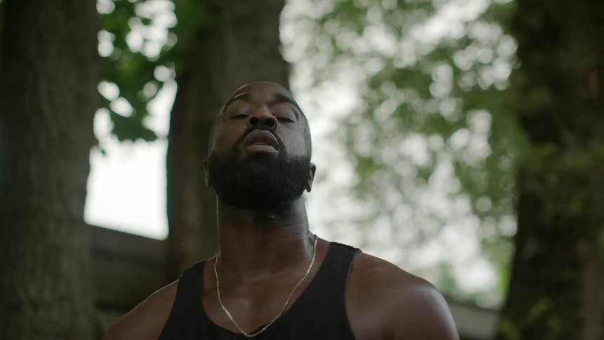 A man standing outside and spitting with trees the sky and clouds in the background