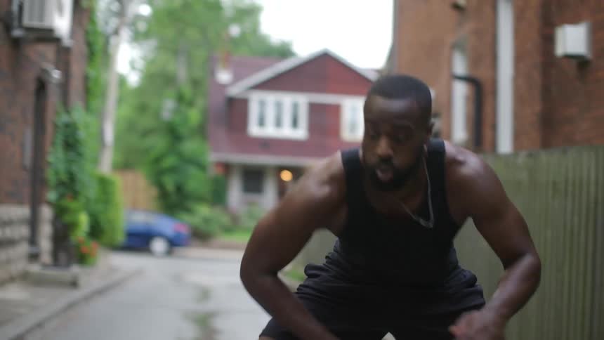 A black man is exercising in an alley between buildings