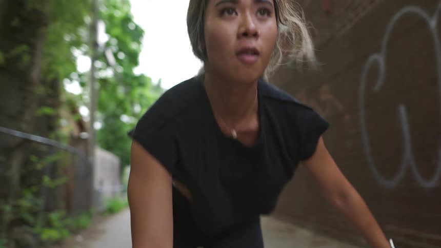 Woman exercises in alley between fenced buildings and brick walled building with graffiti