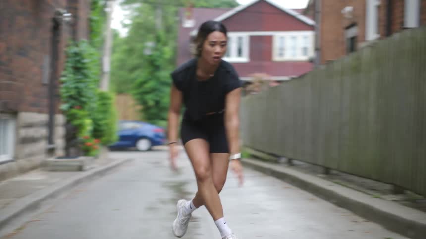 A young woman does exercises in an alleyway in a city neighborhood on a cloudy day